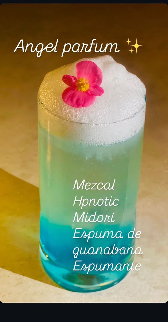 Angel Parfum cocktail, a blue-green layered drink topped with airy foam and a pink flower